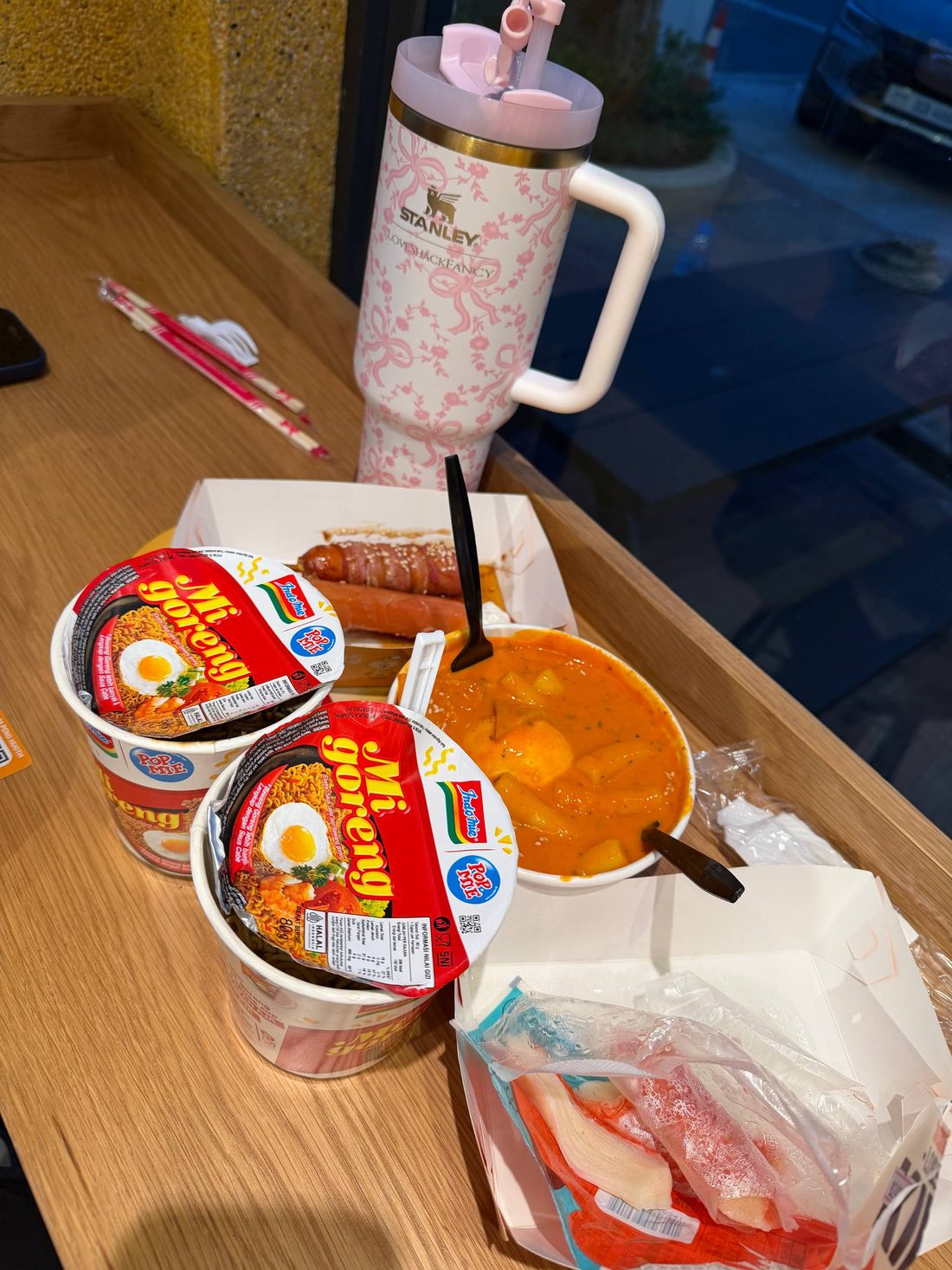 Cup noodles, a sausage box and a bowl of tteokbokki on the counter seating
